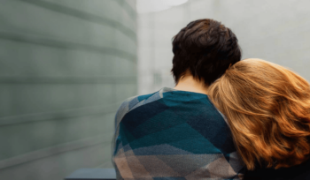 Two people sitting, one with their head on the other's shoulder