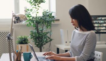 Young Asian woman using laptop in minimalistic office