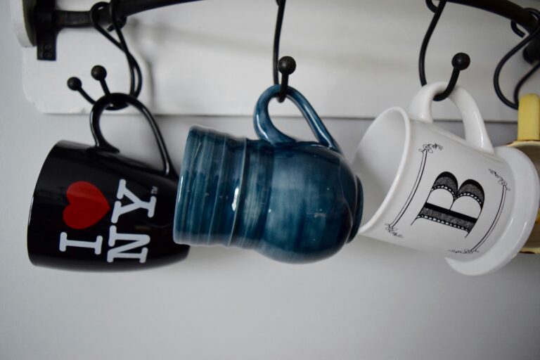 3 different coffee cups hanging by their handles. One says I love NY.