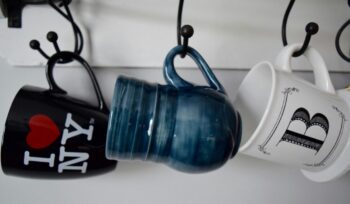 3 different coffee cups hanging by their handles. One says I love NY.