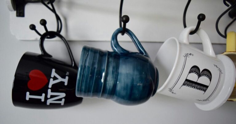 3 different coffee cups hanging by their handles. One says I love NY.