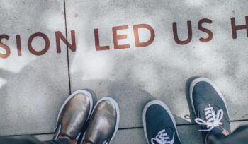 2 pairs of shoes facing a sidewalk with the slogan, Passion led us here