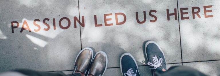 2 pairs of shoes facing a sidewalk with the slogan, Passion led us here